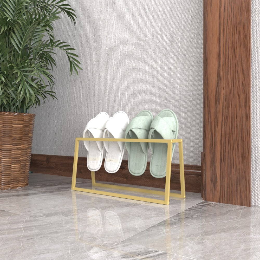 Altın rengi metal bir terliklik, içinde beyaz ve mint yeşili terlikler bulundurarak modern bir dokunuş sağlıyor; ahşap bir duvarın ve mermer zeminin yanında konumlandırılmış.