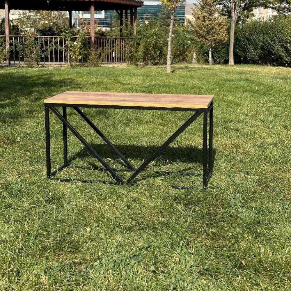 Dış mekanda, yeşil bir çim üzerinde duran, ahşap tablası ve V şeklinde tasarıma sahip, boş siyah metal bir odunluk.