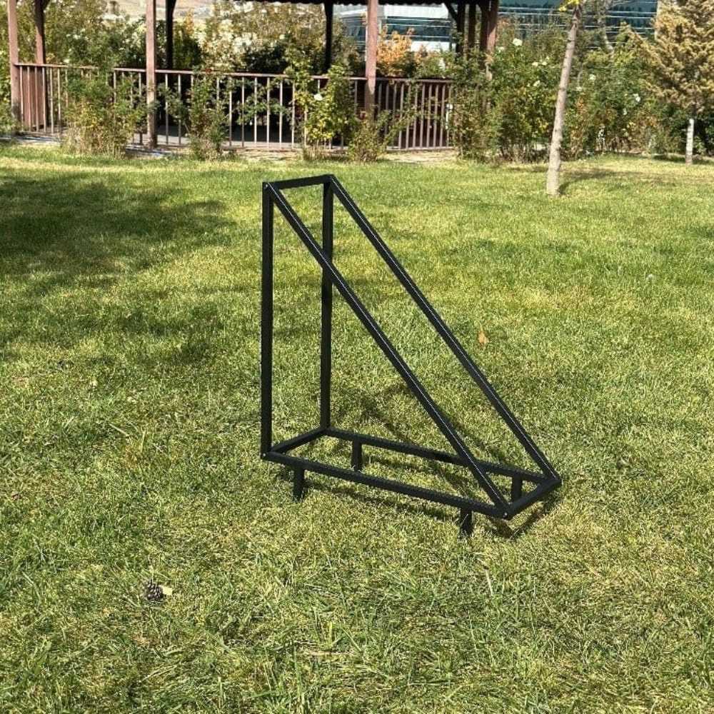 Dış mekanda, çimenlik bir alana yerleştirilmiş, doğal ışık altında sağlam ve minimalist yapısını sergileyen, boş siyah üçgen metal bir odunluk.