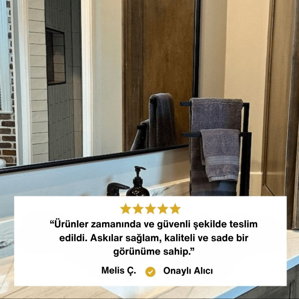 Modern bir banyoda tezgâh üzerine yerleştirilmiş siyah metal havluluk üzerinde gri havlular sergilenmektedir. Alt bölümde müşteri yorumu yer alır: “Ürünler zamanında ve güvenli şekilde teslim edildi. Askılar sağlam, kaliteli ve sade bir görünüme sahip.” Yorum “Melis Ç. - Onaylı Alıcı” olarak belirtilmiştir.