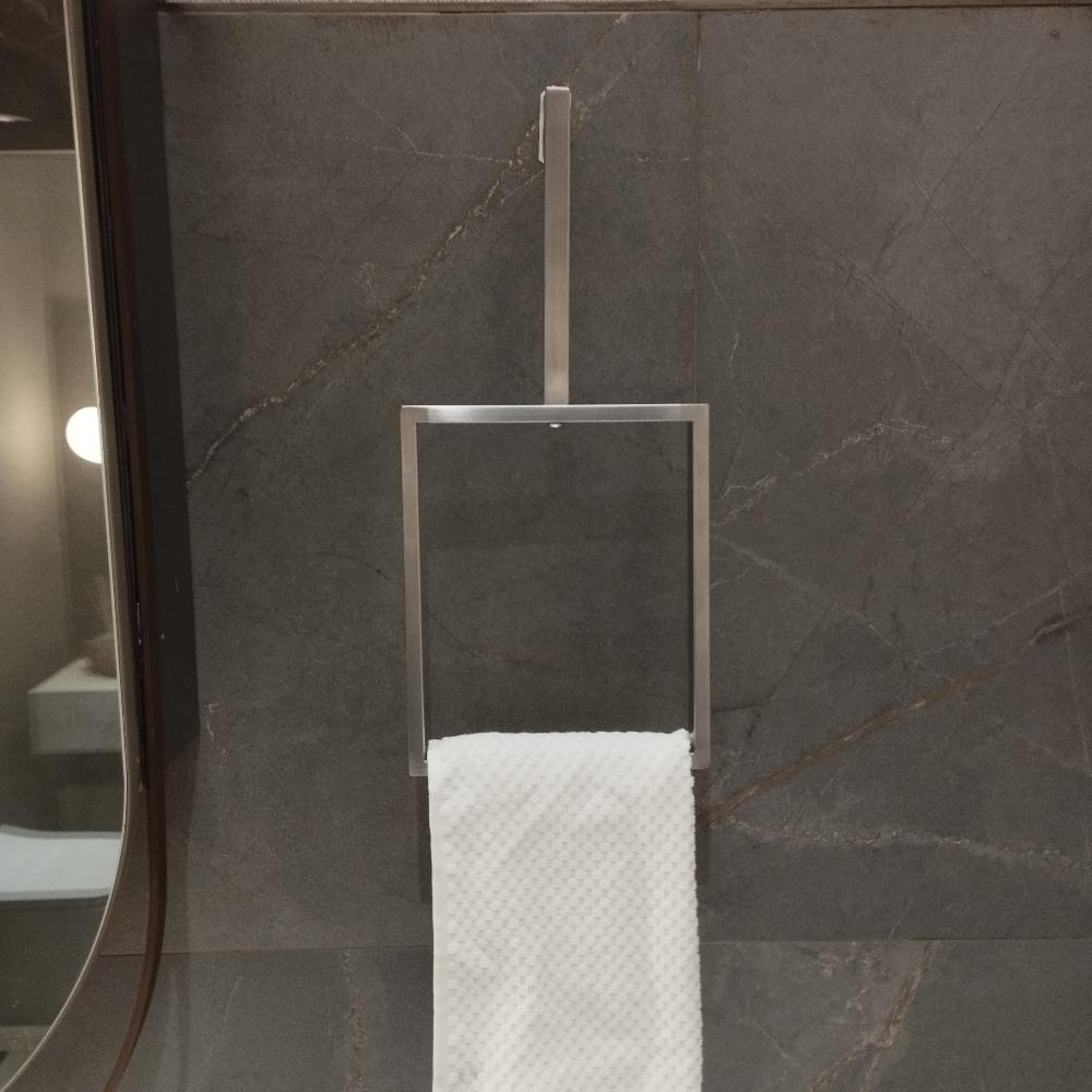 Koyu taş bir duvara monte edilmiş, saten nikel kaplamalı minimalist dikey bir havlu halkası. Şık, dikdörtgen tasarım, beyaz dokulu bir havluyu tutarak banyo dekoruna modern bir dokunuş katıyor. Havlu halkasının sade ama zarif tasarımı, mekanın sofistike atmosferini tamamlıyor.