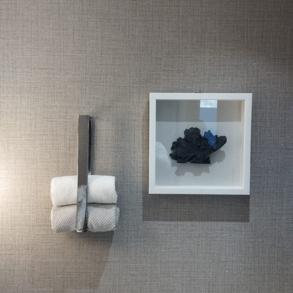 Gri bir banyo duvarına monte edilmiş, gri bir havluyu tutan, arka planda ahşap raflar ve modern aydınlatma bulunan siyah altıgen şeklinde bir havlu halkası.