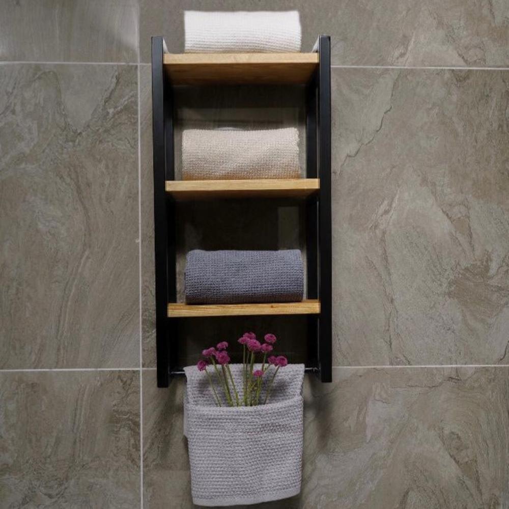Taş dokulu bir duvara monte edilmiş üç raflı banyo havluluğu. Düzenleyici, siyah metal çerçevelere ve ahşap raflara sahip olup, katlanmış bej ve gri havluları sergilemektedir.