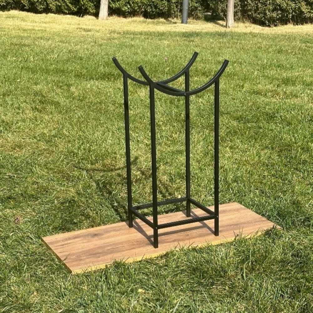 Minimalist siyah metal kütük ve tutuşturucu rafı, benzersiz kavisli üst tasarımıyla dış mekanda ahşap bir platform üzerine yerleştirilmiş, yemyeşil bir çimle çevrilidir.