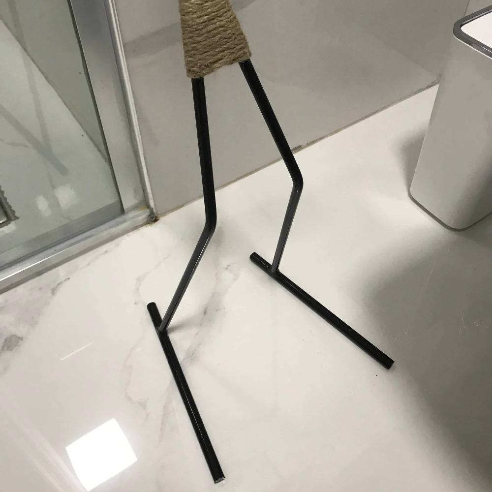 Beyaz mermer bir banyo zemininde gösterilen, minimalist figür şeklinde bir tuvalet kağıdı tutucunun siyah metal tabanının yakın çekimi.
