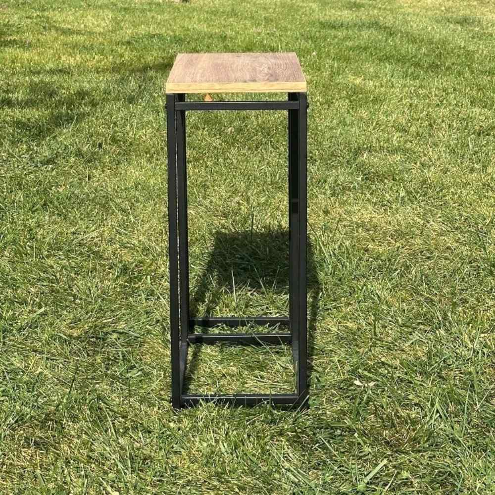 Dış mekanda, çimlerin üzerine yerleştirilmiş, dar derinliği ve çağdaş tarzını vurgulayan, ahşap tablası olan minimalist siyah metal bir odunluğun yan görünümü.