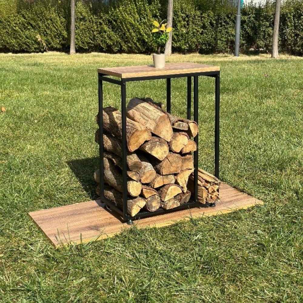 Dış mekanda, çimlerin üzerine yerleştirilmiş, istiflenmiş odun ve çıra tutan, ahşap tablası olan minimalist siyah metal bir odunluk.