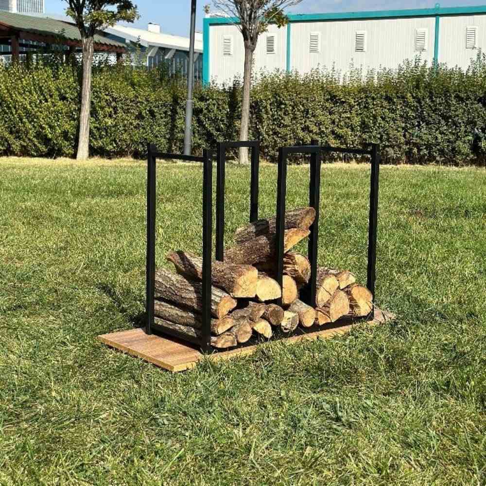 Dış mekanda, ahşap bir taban üzerinde duran, içine kesilmiş kütükler ve çıra doldurulmuş, siyah metal bir odunluk, aynı zamanda çıra depolama alanına da sahip.