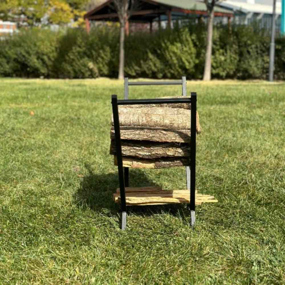 Yemyeşil çimlerin üzerinde, dış mekanda yer alan, düzenli bir odun istifi tutan ve küçük kütükler için alt bölmesi bulunan siyah V şeklinde bir odunluğun önden görünümü.