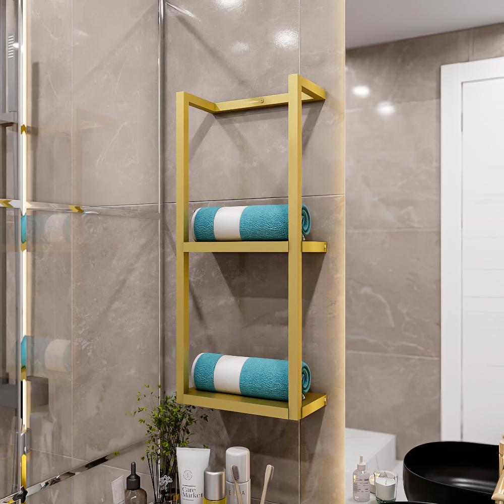 Her bir katında düzenli bir şekilde rulo yapılmış teal havlular bulunan, bej fayanslı bir duvara, çeşitli banyo malzemeleri bulunan bir tezgahın üzerine monte edilmiş iki katlı altın metal banyo rafı.
