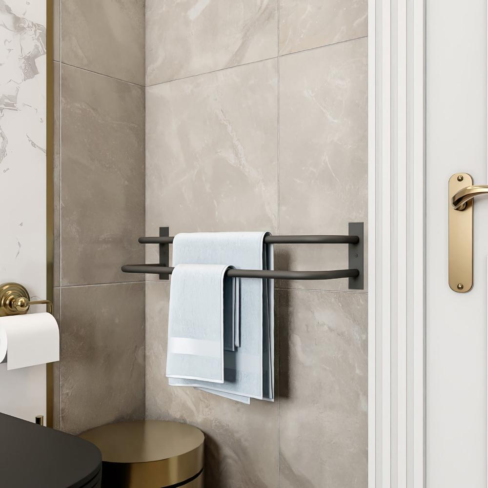 Temiz ve minimalist bir banyo ortamında, duvara monte edilmiş siyah çift barlı havluluk, düzenli katlanmış mavi havluları tutuyor. Fayansların nötr tonları ve altın rengi kapı kolu, genel tasarıma zarif bir dokunuş katıyor.