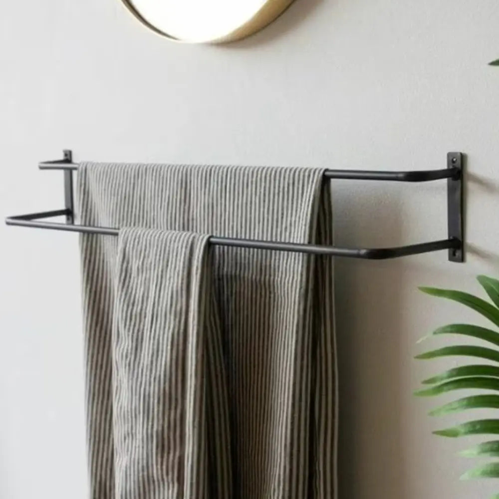 Siyah havluluğun minimalist bir banyoda, dokulu bir duvar ve dairesel bir ayna fonunda çizgili havlularla monte edilmiş yakın çekimi. Yeşil bitkiler, temiz ve modern tasarıma ferahlatıcı bir dokunuş katıyor.