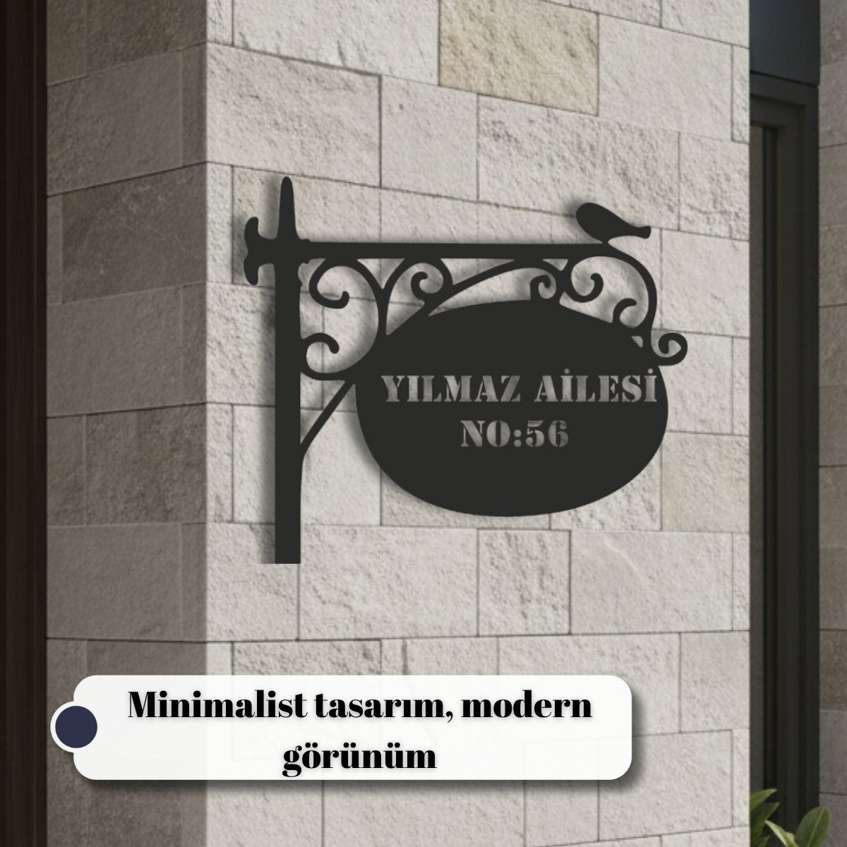 Klasik ferforje tasarımıyla dairesel bir isimlik alanını birleştiren, üzerinde minik bir kuş figürü bulunan siyah metal duvar dekoru.