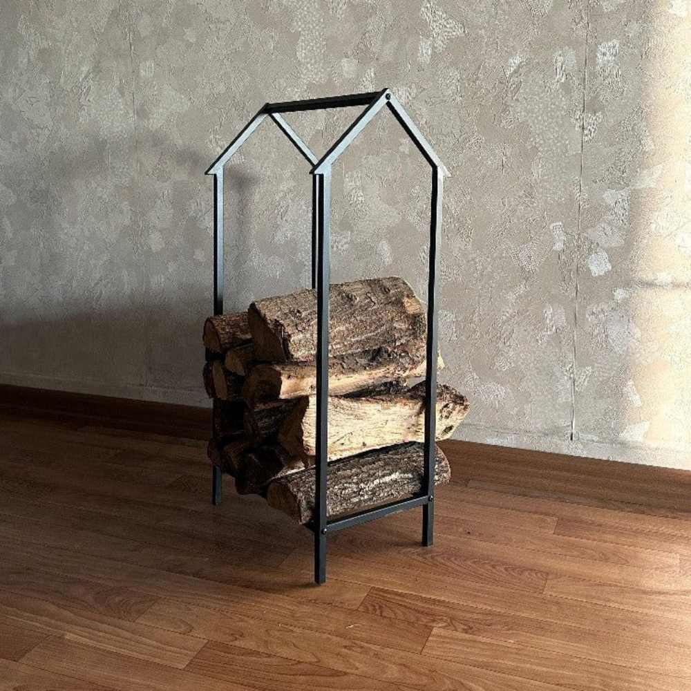 Dokulu bir duvar arka planı olan sıcak ahşap bir zeminde sergilenen, içine düzenli bir şekilde kütüklerin istiflendiği, minimalist ev şeklinde tasarlanmış kompakt metal bir odunluk.