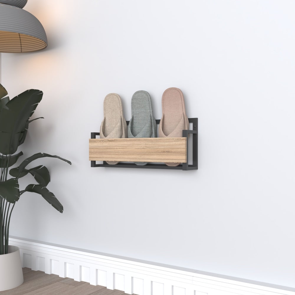 Şık siyah metal çerçeveli ve ahşap ön yüzlü modern, duvara monte bir terlik rafı; üç çift pastel renkli terlik barındırıyor ve saksı bitkileri ile duvar dekorasyonuna sahip minimalist bir odada konumlandırılmış.