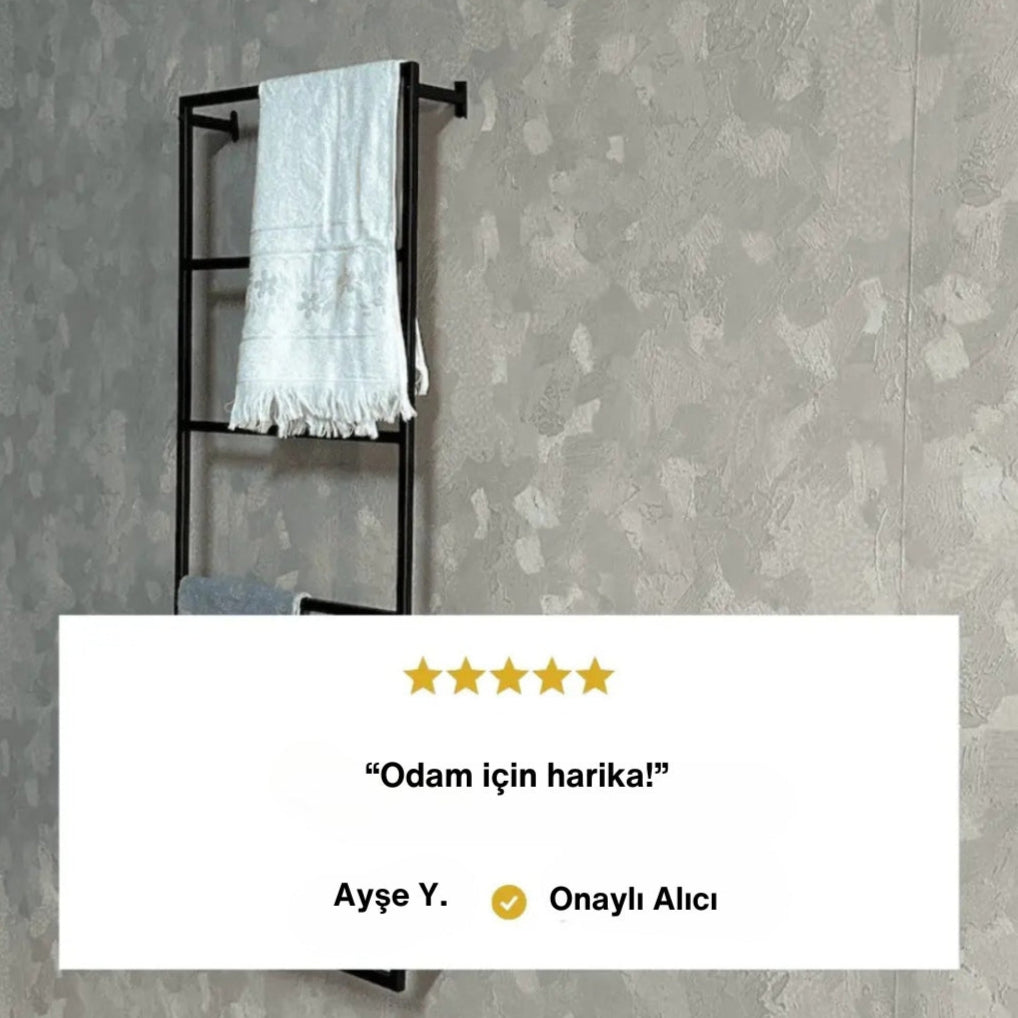 Duvara monte edilmiş siyah metal havluluk üzerinde beyaz ve gri havlular asılıdır. Alt kısımda beş yıldızlı müşteri yorumu yer alır: “Odam için harika!” Yorumun altında “Ayşe Y. - Onaylı Alıcı” ifadesi bulunur.