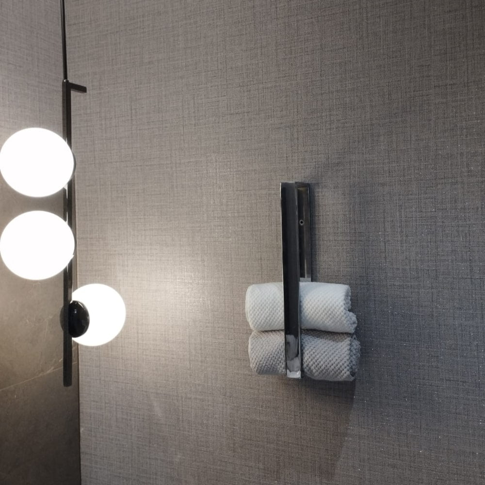 Gri bir banyo duvarına monte edilmiş, gri bir havluyu tutan, arka planda ahşap raflar ve modern aydınlatma bulunan siyah altıgen şeklinde bir havlu halkası.