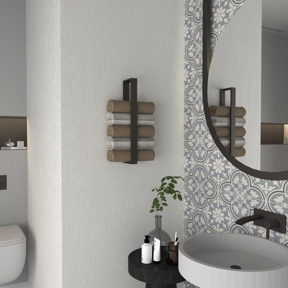 Şık ve fonksiyonel bir tasarım yaratan, desenli fayanslı yuvarlak bir aynanın yanına monte edilmiş, düzenli bir şekilde rulo yapılmış havluları tutan mat siyah minimalist dikey havluluklu bir banyo.